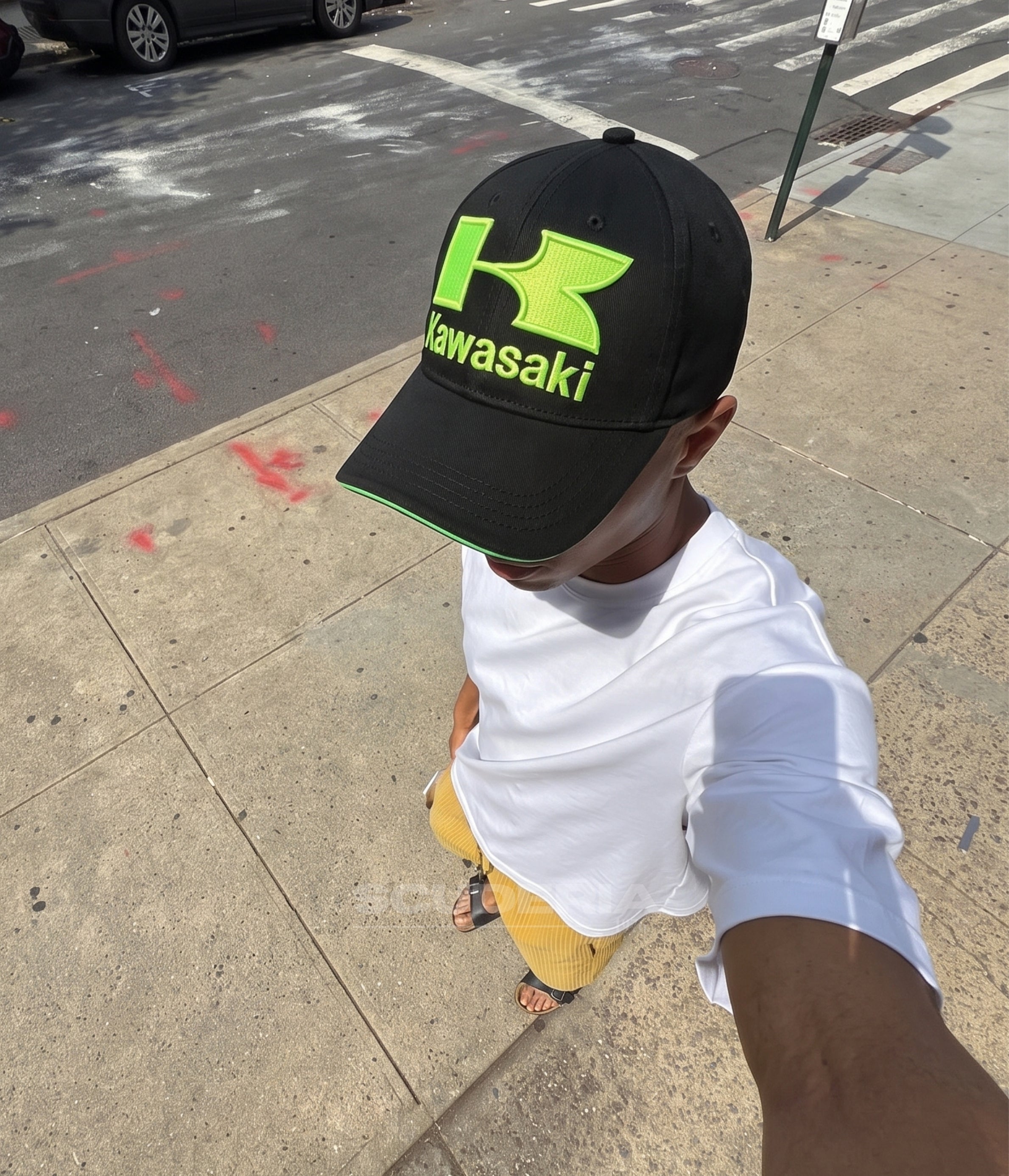 Man wearing the black Kawasaki Racing cap on a city sidewalk