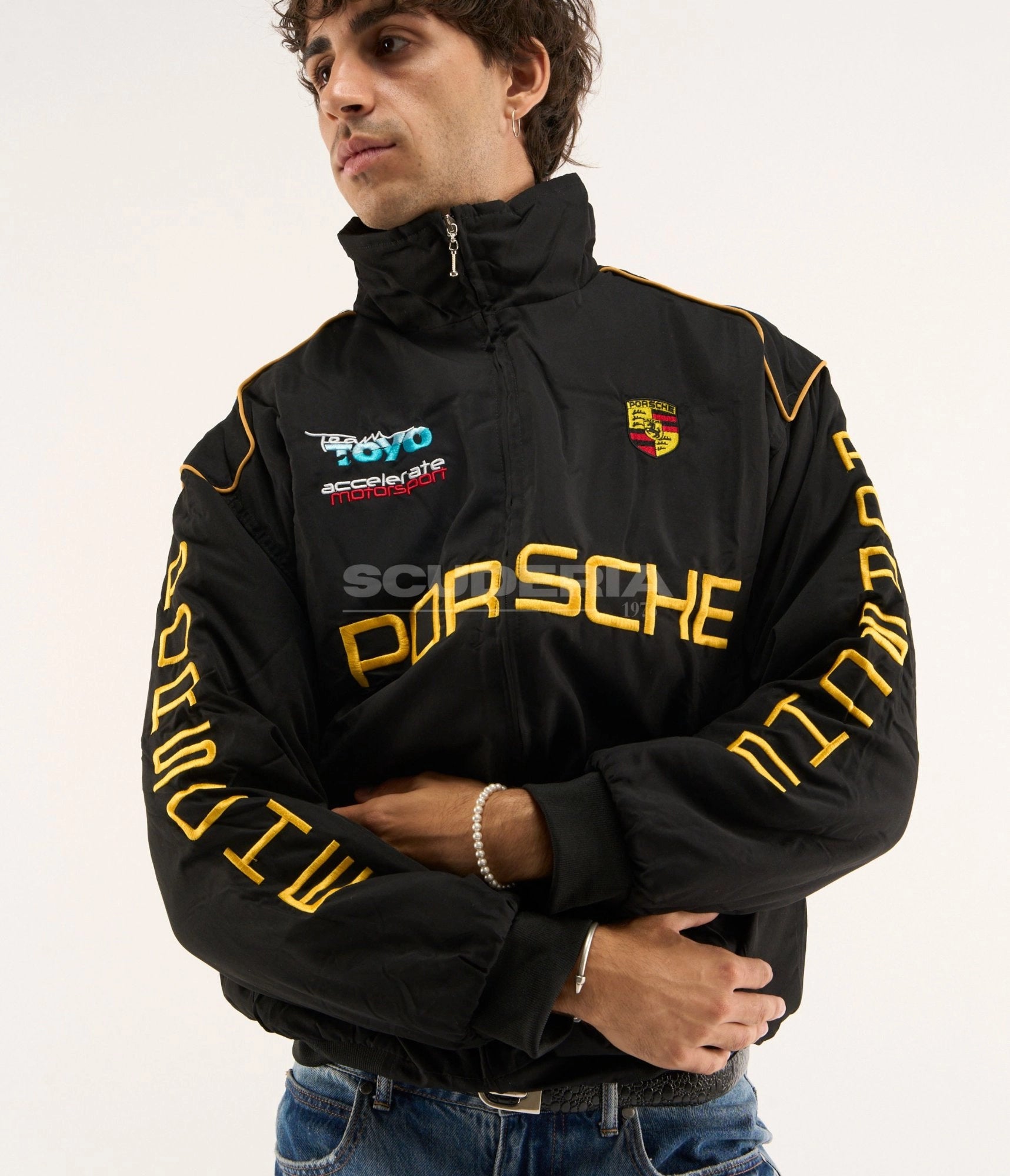 Porsche Vintage Racing Jacket black gold crossed arms front view men – vintage padded bomber with gold embroidered Porsche logo, Porsche crest, Team Toyo Accelerate Motorsport patch, gold sleeve lettering