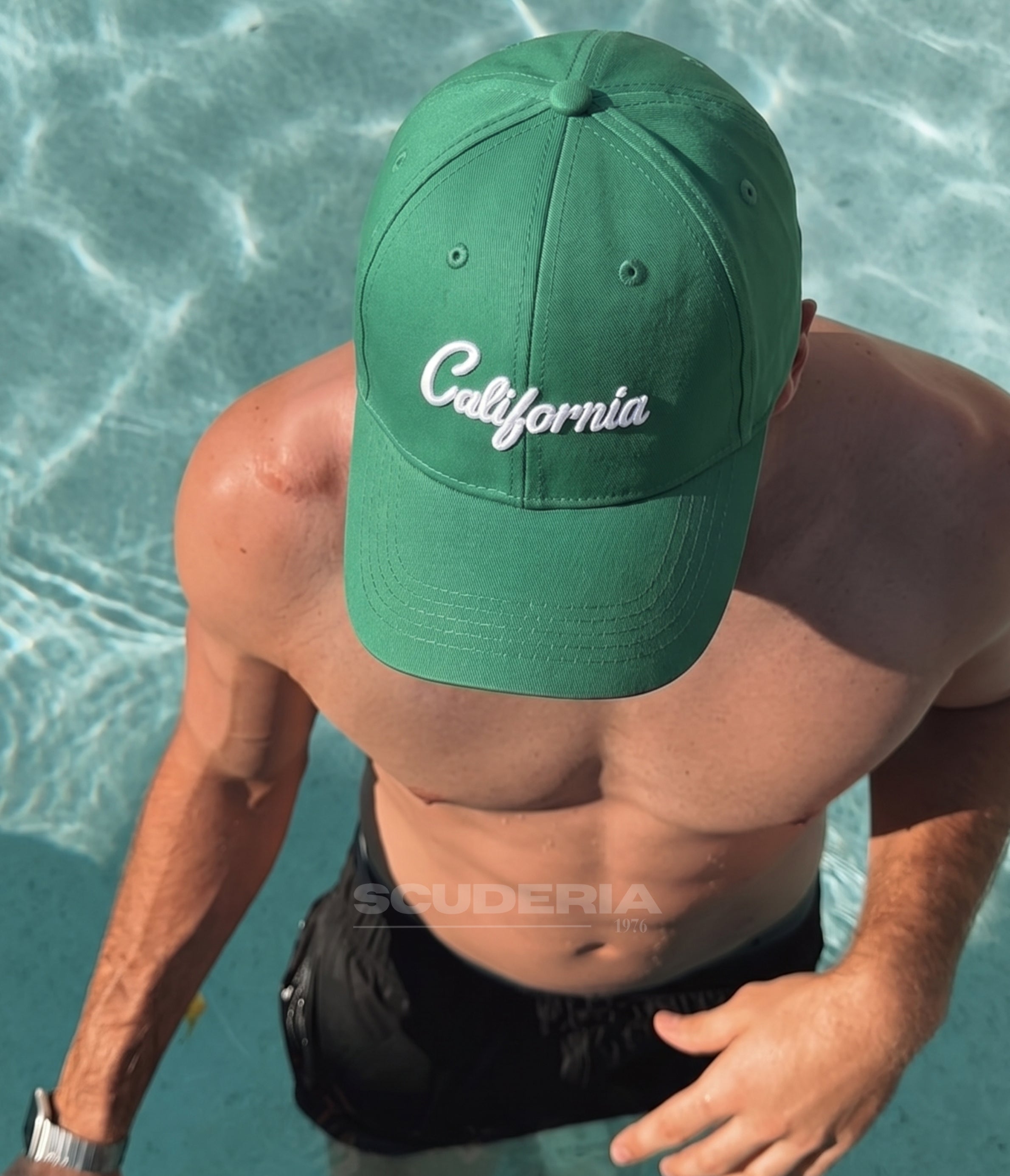 Man wearing the green California cap by a swimming pool
