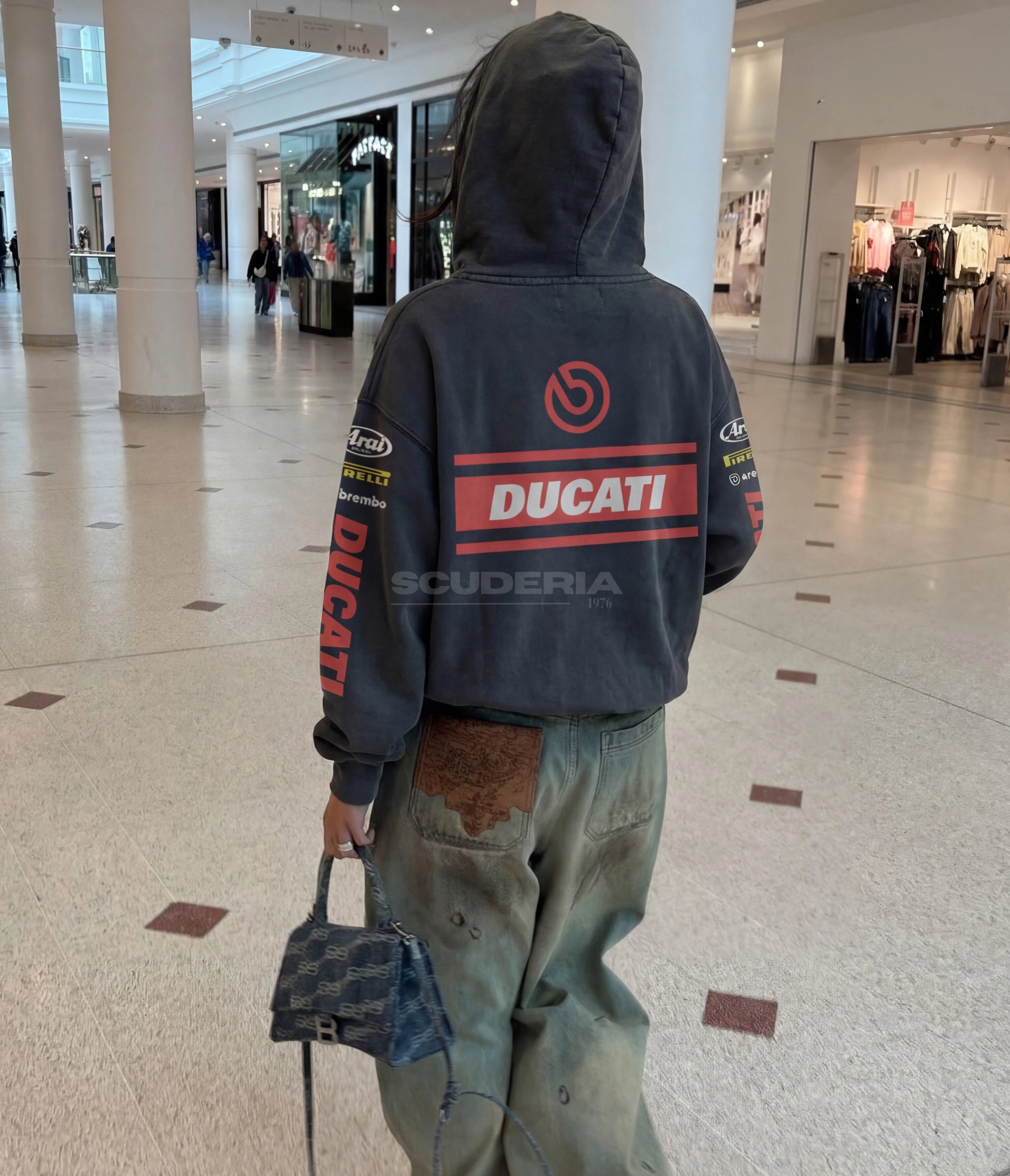 Ducati Brembo Racing Hoodie black washed lifestyle back view women – vintage oversized motorsport sweatshirt styled with baggy distressed cargo pants and mini bag, Ducati red banner back graphic, Brembo logo, Arai Pirelli sleeve sponsors, mall street style look