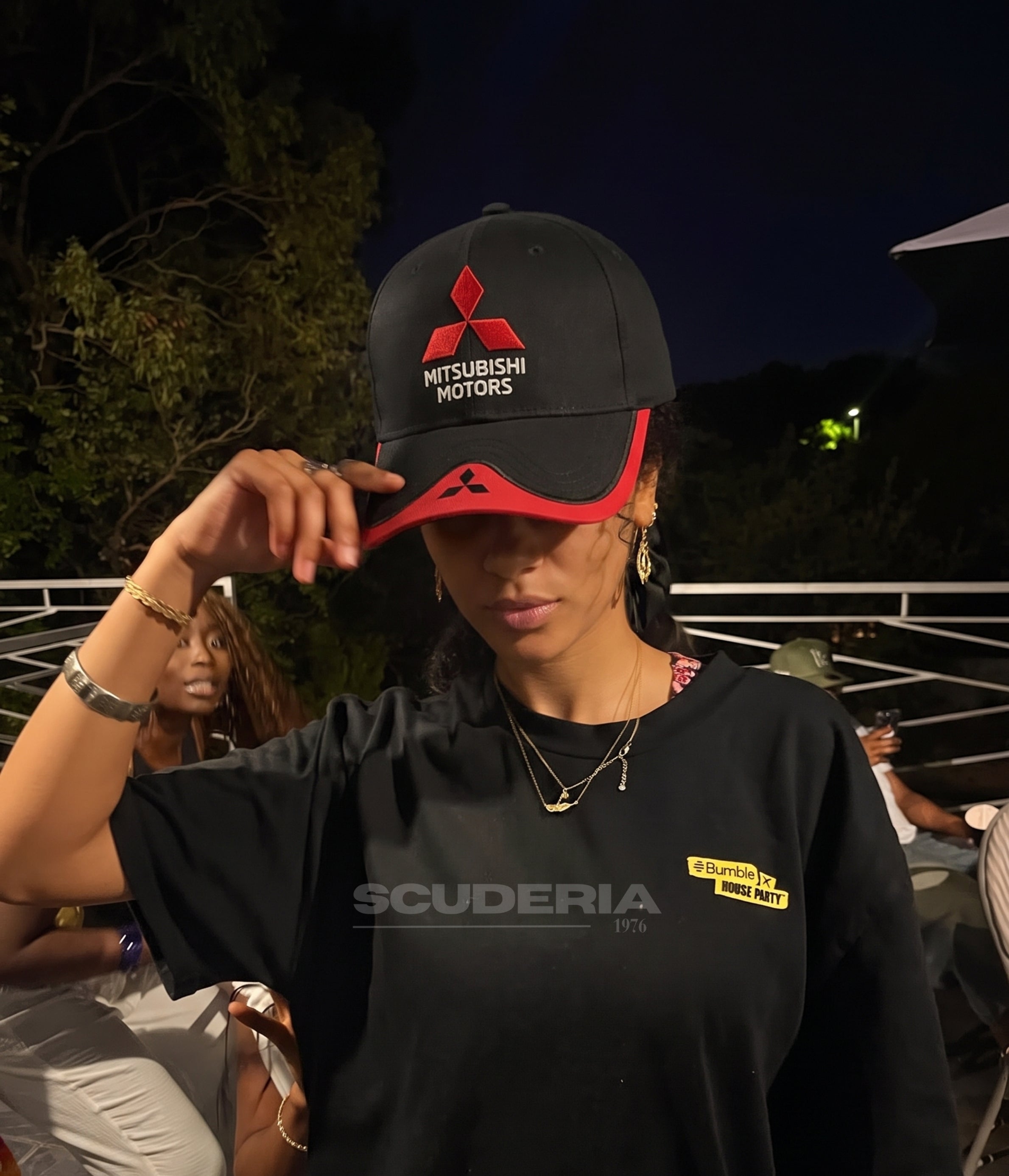 Woman wearing the black and red Mitsubishi Motors cap at night