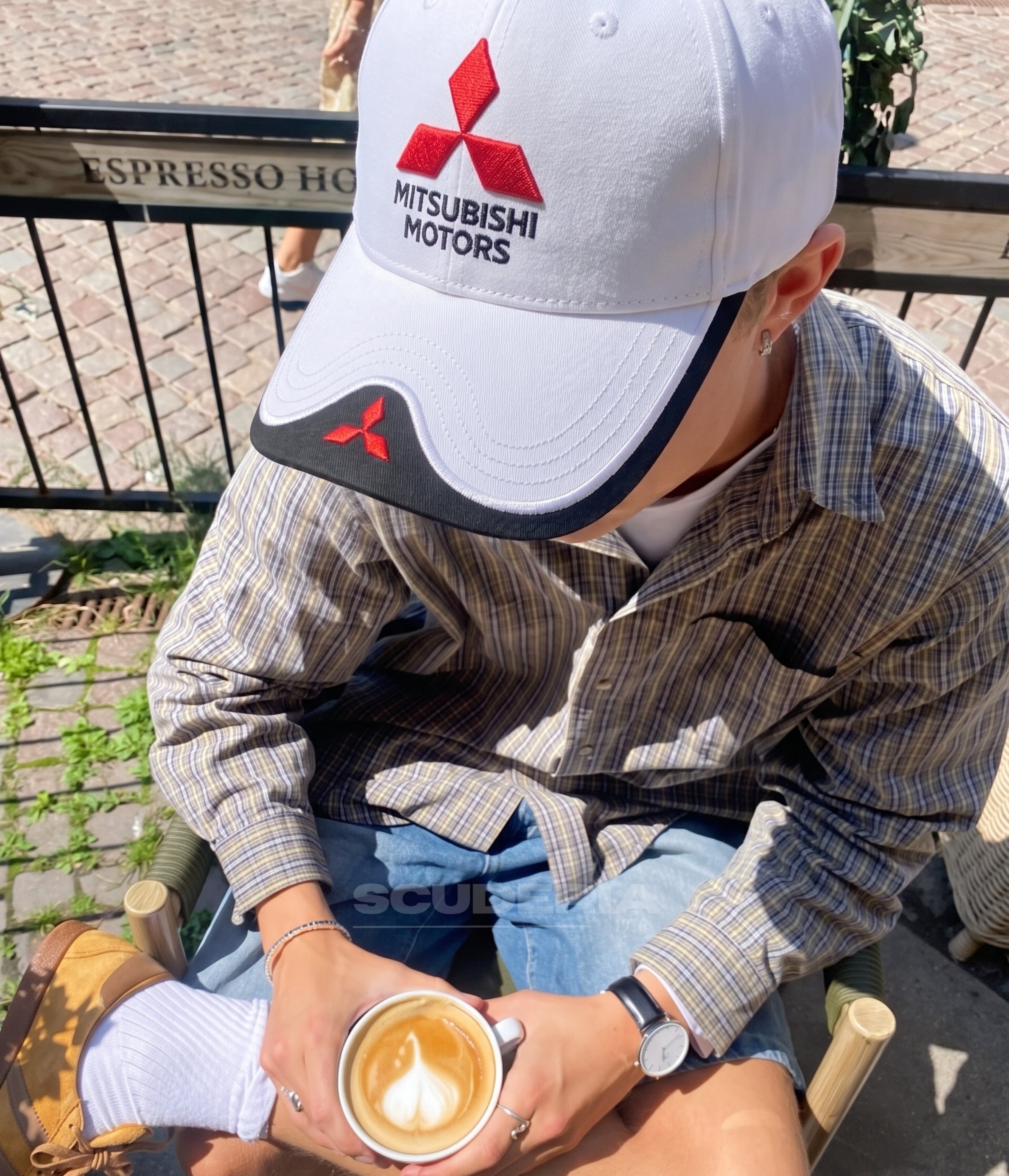 Man wearing the white Mitsubishi Motors cap on a cafe terrace with a coffee